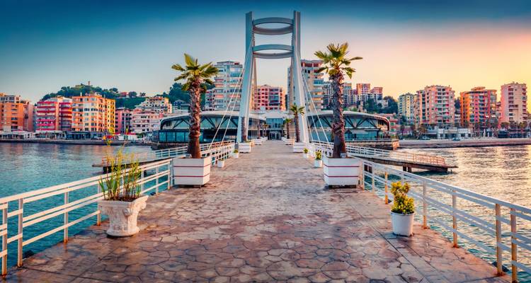 Sunset promenade lined with palm trees leading to a modern bridge on Vlore's Adriatic waterfront.