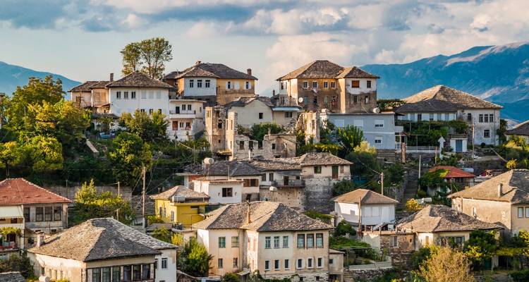 Stone Ottoman-style houses cascade down a hillside in the historic old town with distant mountains and dramatic skies.
