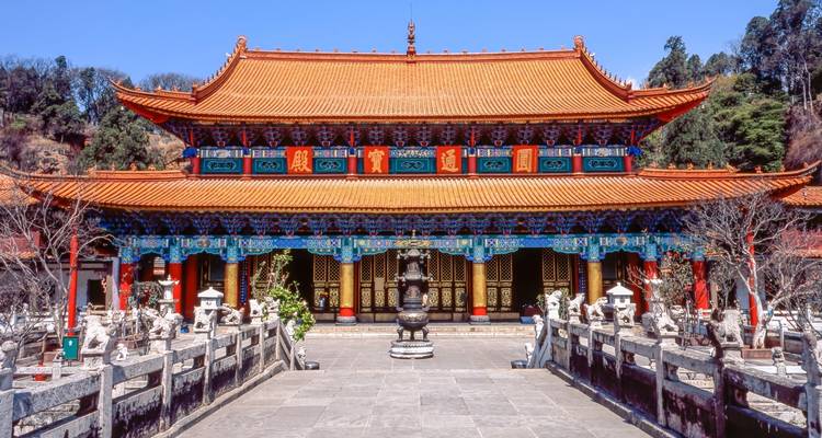 Un temple du Yunnan coloré aux bannières éclatantes et aux balustrades en pierre sculptée se dresse sous un ciel dégagé.