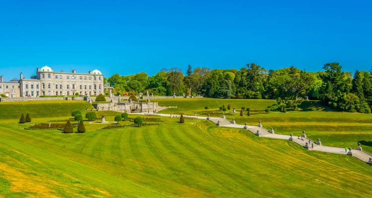De larges terrasses vertes et des jardins formels menant à la grandiose maison Palladian Powerscourt sous des ciels d'un bleu cristallin.
