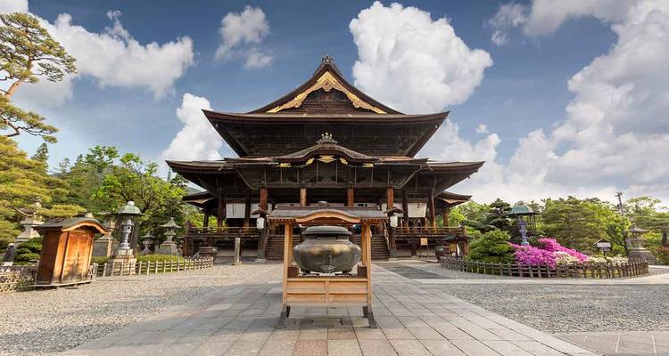 Front view of Zenko-ji Temple in Nagano against a blue sky with fluffy clouds.