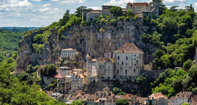 Village spectaculaire de Rocamadour perché sur les falaises avec ses bâtiments en pierre et une vallée boisée en contrebas par une journée partiellement nuageuse.