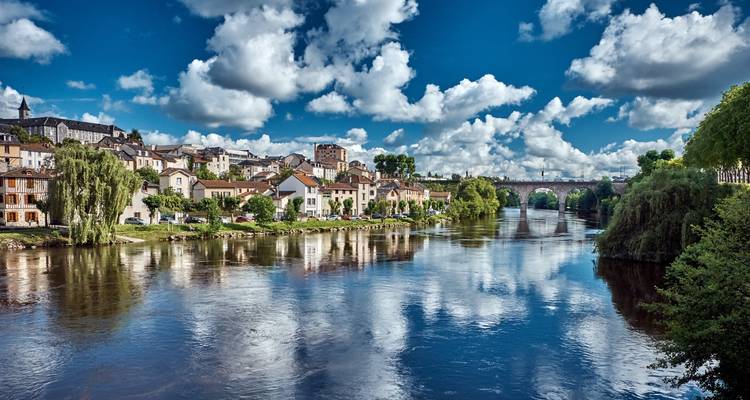 Rivière calme reflétant une rangée de maisons et un pont en pierre sous un ciel bleu profond avec des nuages cotonneux à Limoges.