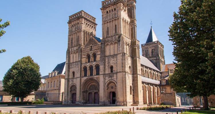 Église abbatiale en pierre romane avec deux tours carrées jumelles sous un ciel bleu