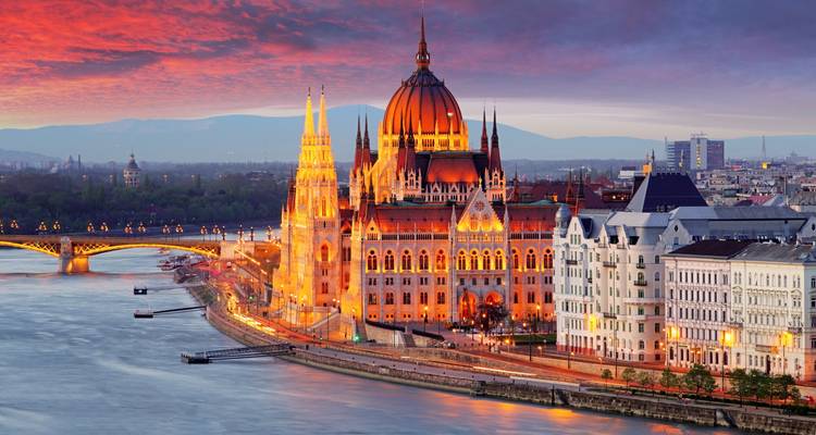 Illuminated Hungarian Parliament Building and Fisherman’s Bastion glow at sunset beside the Danube River in Budapest.