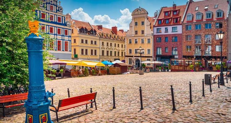 Lebhafter Marktplatz mit farbenfrohen Fassaden, Sonnenschirmen und Aussencafes unter blauem Himmel.