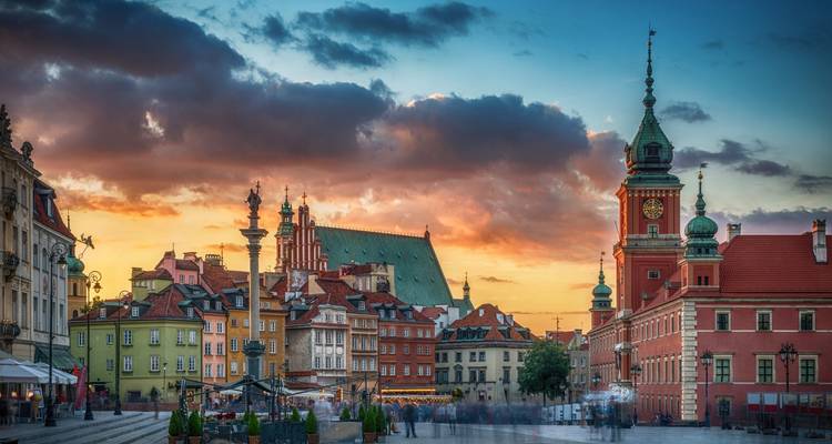Der lebhafte Warschauer Schlossplatz bei Sonnenuntergang mit farbenfrohen historischen Gebäuden und dramatischem Himmel.