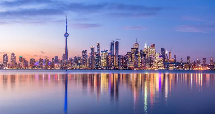 Skyline de Toronto illuminée au crépuscule, reflets colorés des bâtiments scintillant sur l'eau calme du lac