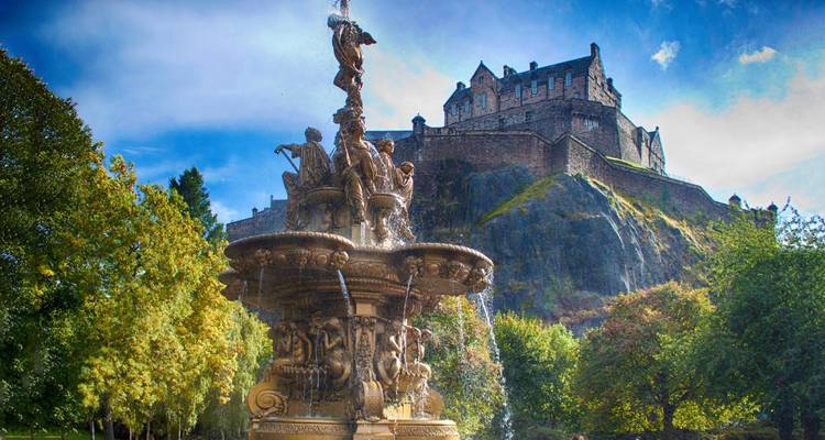 Sunny view of Ross Fountain with Edinburgh Castle perched high on a rocky hill behind.