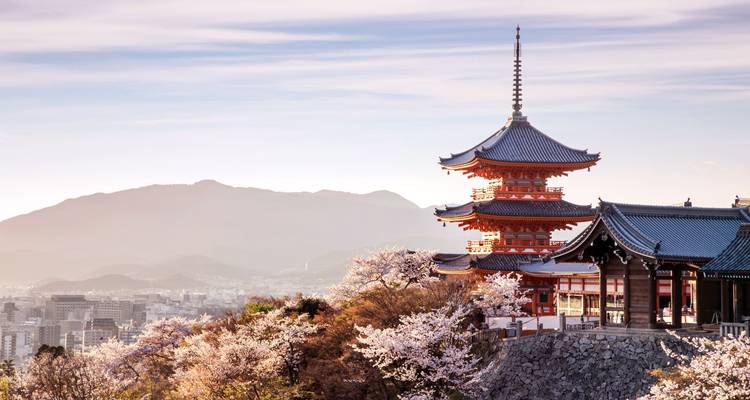 Hilltop pagoda surrounded by cherry blossoms with a hazy mountain backdrop at dawn.