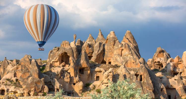 Hot-air balloon floats above the surreal rock formations and cave dwellings of Cappadocia at dawn