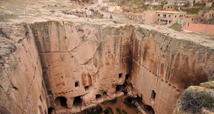 View into a deep rectangular rock-cut monastery with multiple cave rooms and eroded walls