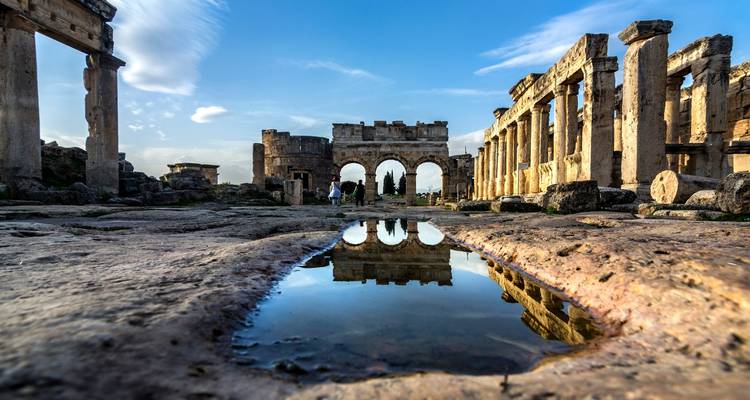 Ancient stone gate and colonnaded ruins of Hierapolis reflected in a rain puddle at Pamukkale