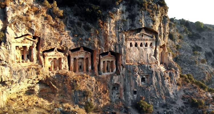 Ancient Lycian rock-cut tomb facades embedded high in a cliff face at sunset light