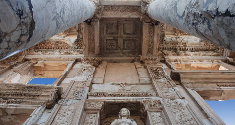 Upward perspective between marble columns to ornate ceiling of the Library of Celsus