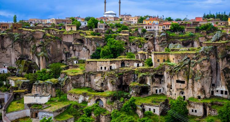 Cliffside village with rock-cut dwellings overgrown with greenery, a mosque rising above