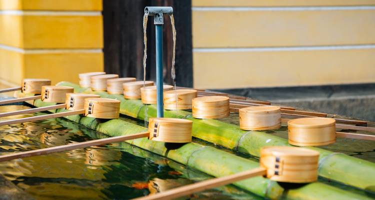 Rangées de louches en bois à une fontaine de purification en bambou dans la cour d'un sanctuaire japonais.