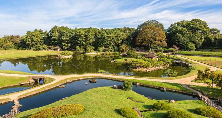 Vue panoramique du Jardin Korakuen avec ses sentiers sinueux, ses étangs et ses espaces verts entretenus sous un ciel bleu.