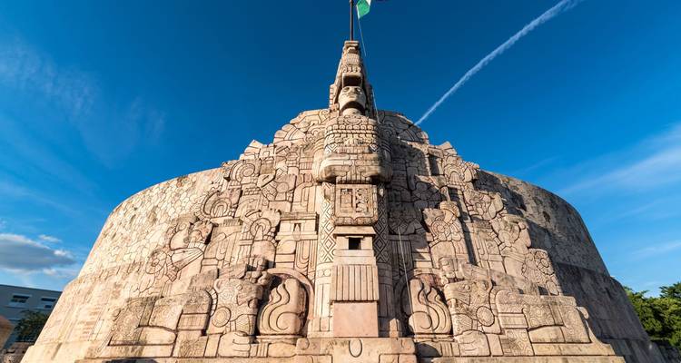 Stone Monumento a la Patria in Merida adorned with intricate Mayan carvings under a vivid blue sky.