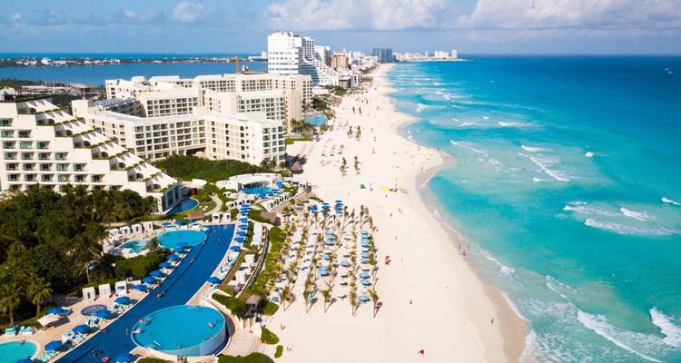 Long stretch of Cancun’s white sand beach lined with resort hotels and vibrant turquoise water.