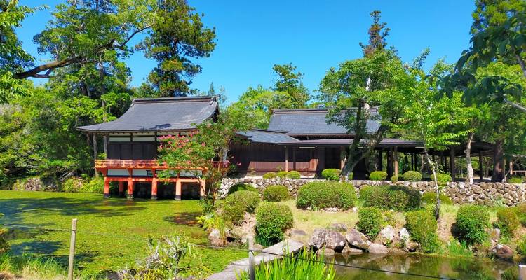 Traditionelle japanische Villa, umgeben von üppigen Gärten und einem Teich, der mit grünem Entenflott bedeckt ist.