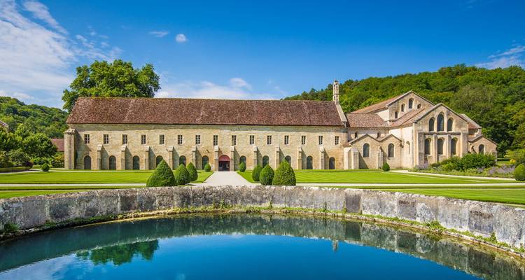 Peaceful view of Fontenay Abbey reflected in a circular pond amid manicured lawns and forest backdrop.