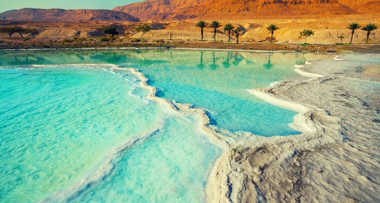 Des bassins turquoise éclatants et des terrasses de sel blanc du rivage de la mer Morte avec des montagnes désertiques au-delà.