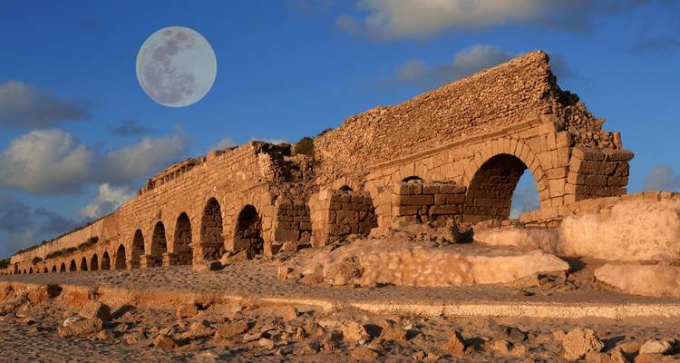 Antike römische Aquädukt-Bögen in Caesarea leuchten im schwachen Licht mit einem großen Mond am Himmel.