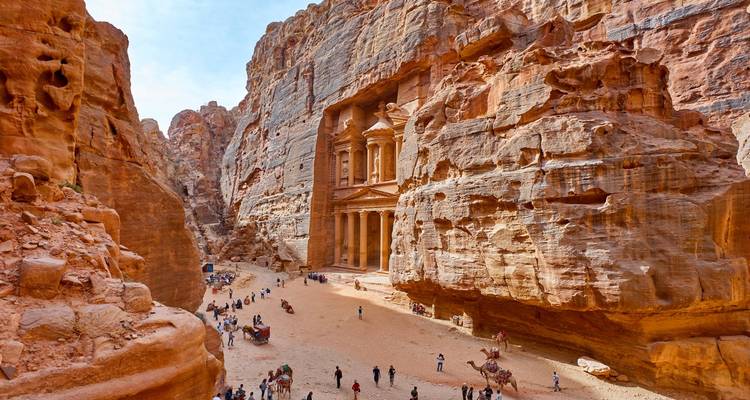 Overdag uitzicht op het Schatkuis in Petra met bezoekers en kamelen aan de voet, gezien tussen de canyonwanden.