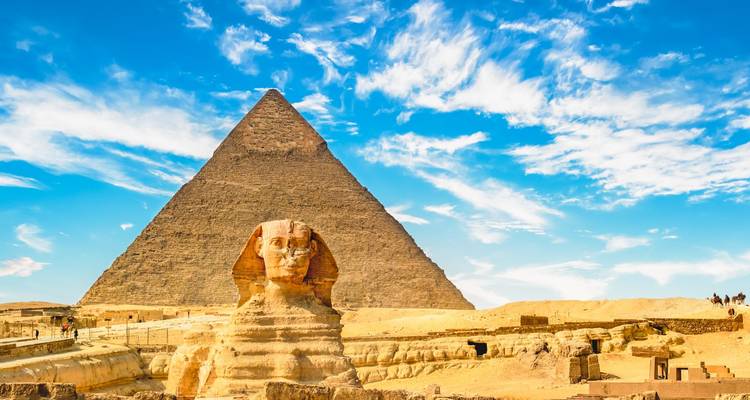 Große Pyramide von Giza mit der Sphinx im Vordergrund unter einem hellen blauen Himmel mit zarten Wolken.
