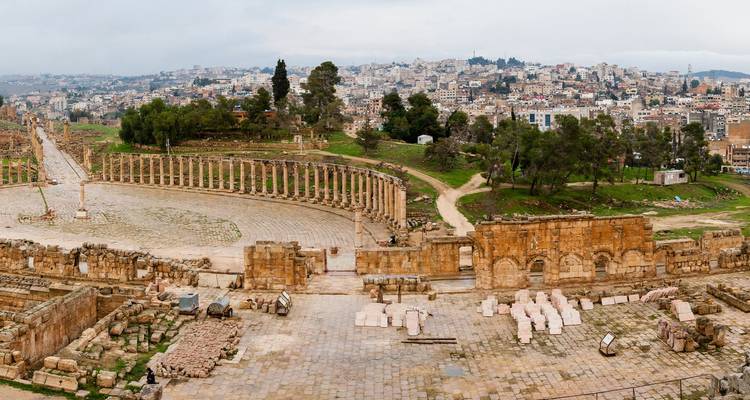 Panoramaaufnahme des Oval Forum und der säulengesäumten Straße der antiken römischen Stadt Jerash mit der modernen Stadt im Hintergrund.