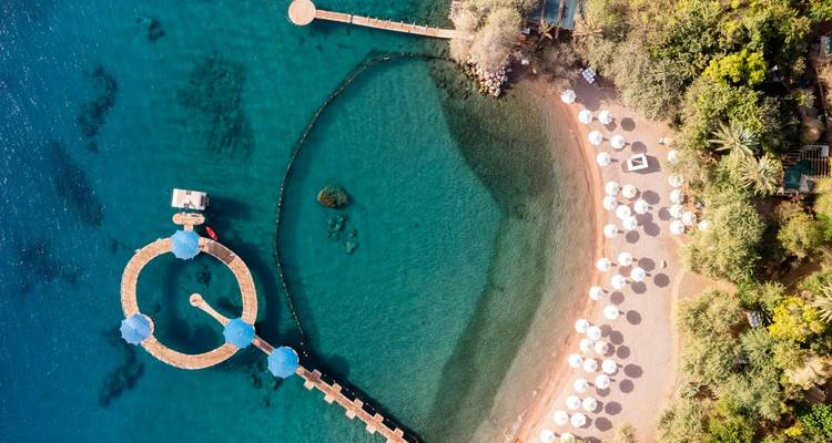 Aerial view of a turquoise bay with circular piers, umbrellas and lush greenery along the shoreline.
