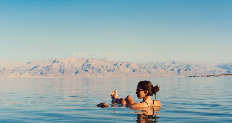 Une femme flottant sans effort dans les eaux flottantes de la mer Morte avec des montagnes arides en arrière-plan.