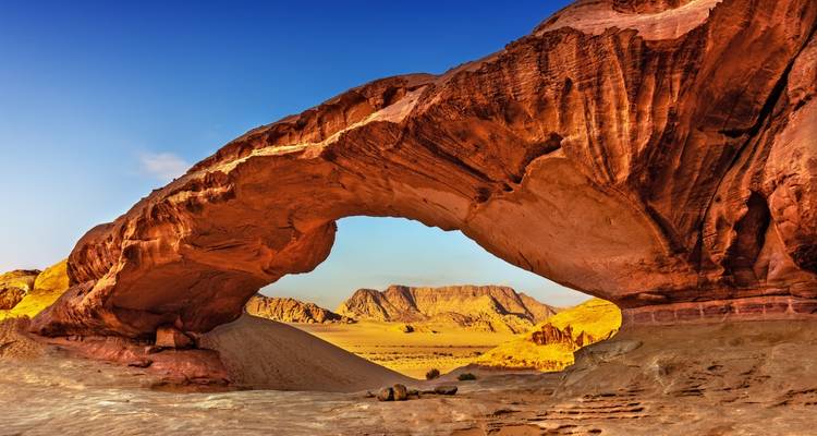 Natürlicher Sandsteinbogen in Wadi Rum, der entfernte Wüstenberge unter einem leuchtend blauen Himmel rahmt.