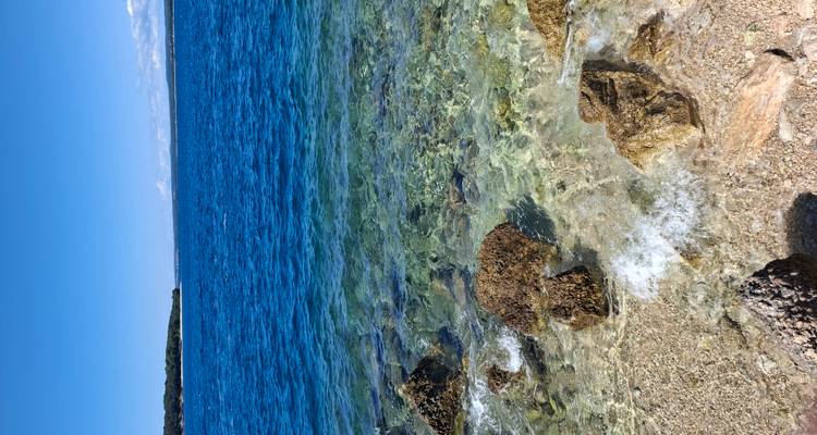 Des teintes bleues cristallines et superposées de la mer avec un rivage rocheux en premier plan sous un ciel lumineux