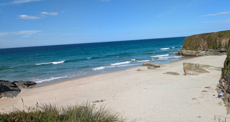 Petite crique sablonneuse tranquille avec des vagues douces et des falaises recouvertes de verdure