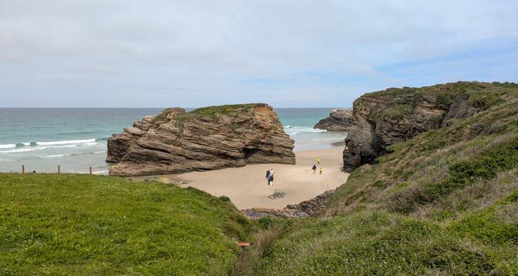 Petit groupe explorant une petite baie sablonneuse entourée de formations rocheuses spectaculaires