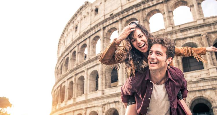 Happy couple piggybacking in front of the Colosseum lit by warm sunlight