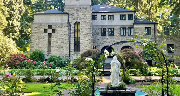 Serene rose garden with white statue before a historic stone monastery building.