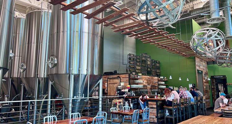 Modern craft brewery interior with towering stainless steel tanks, wood tables, and patrons.