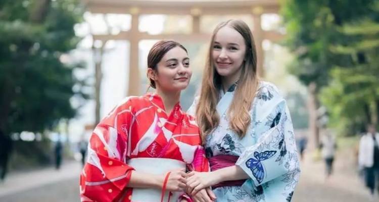 Zwei Frauen in gemusterten Yukatas, die auf einem blättrigen Schreinweg posieren.