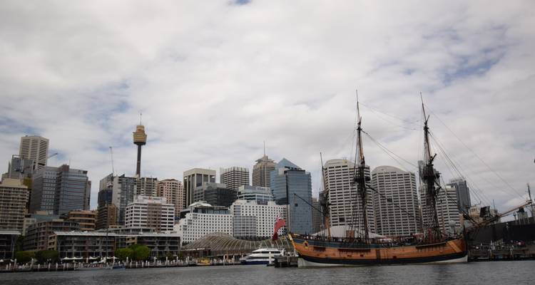 Historic tall ship moored in Darling Harbour with Sydney skyline behind.