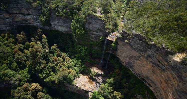 Aerial view of a slender waterfall dropping into a densely forested gorge.