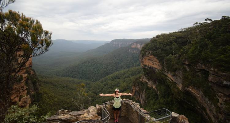 Traveler spreads arms on a rocky lookout with layered valleys behind.