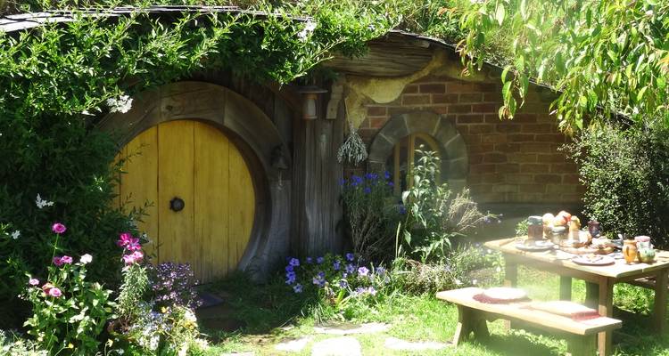 Charming yellow-doored hobbit cottage with garden table laid for a meal among flowers.