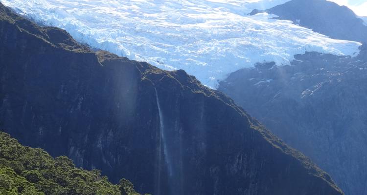 Tall waterfall dropping from a glacier-capped ridge into a deep shadowed valley.