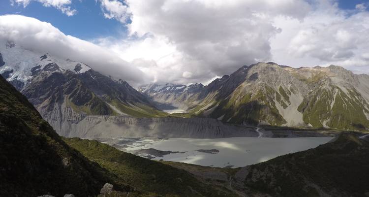 Dramatic glacial valley with milky lakes and steep snow-dusted peaks under mixed clouds.