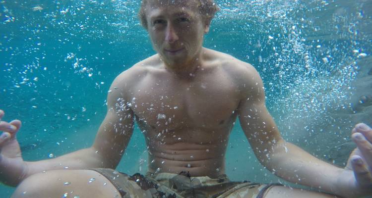 Underwater portrait of a man sitting cross-legged as air bubbles rise around him.