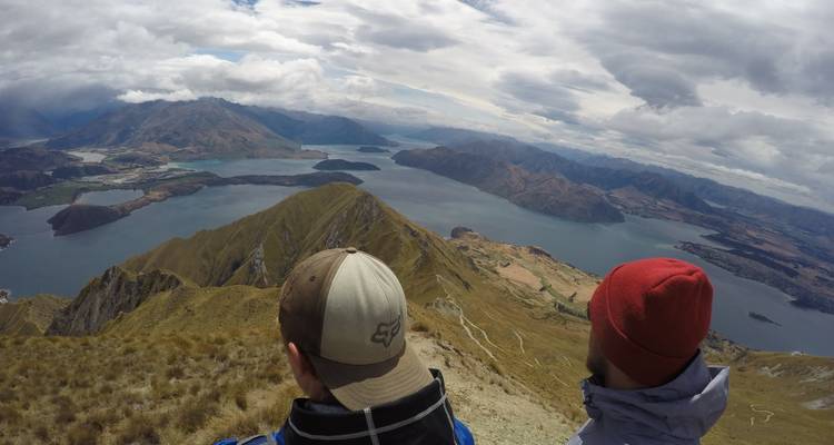 Two hikers look out over lakes and ridgelines from a high alpine summit.
