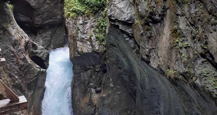 Gorge rocheuse étroite avec des eaux bleues tumultueuses observées depuis une passerelle en bois.